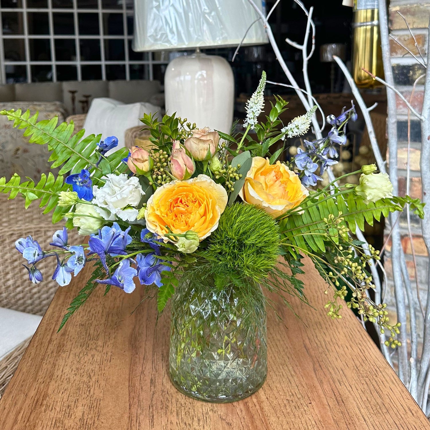 Moss and Daylight floral arrangement by Birch & Blossom with garden roses, delphinium, trick dianthus, white lisianthus, wax flower, Veronica, and mocha spray roses in a clear glass vase. Warm, peaceful, and nature-inspired.