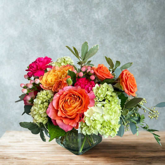 After Glow romantic floral arrangement by Birch & Blossom featuring Free Spirit roses, mini hydrangea, spray roses, carnations, hypericum berries, eucalyptus, leather leaf, and pittosporum in a vase. Fiery tones and lush textures.